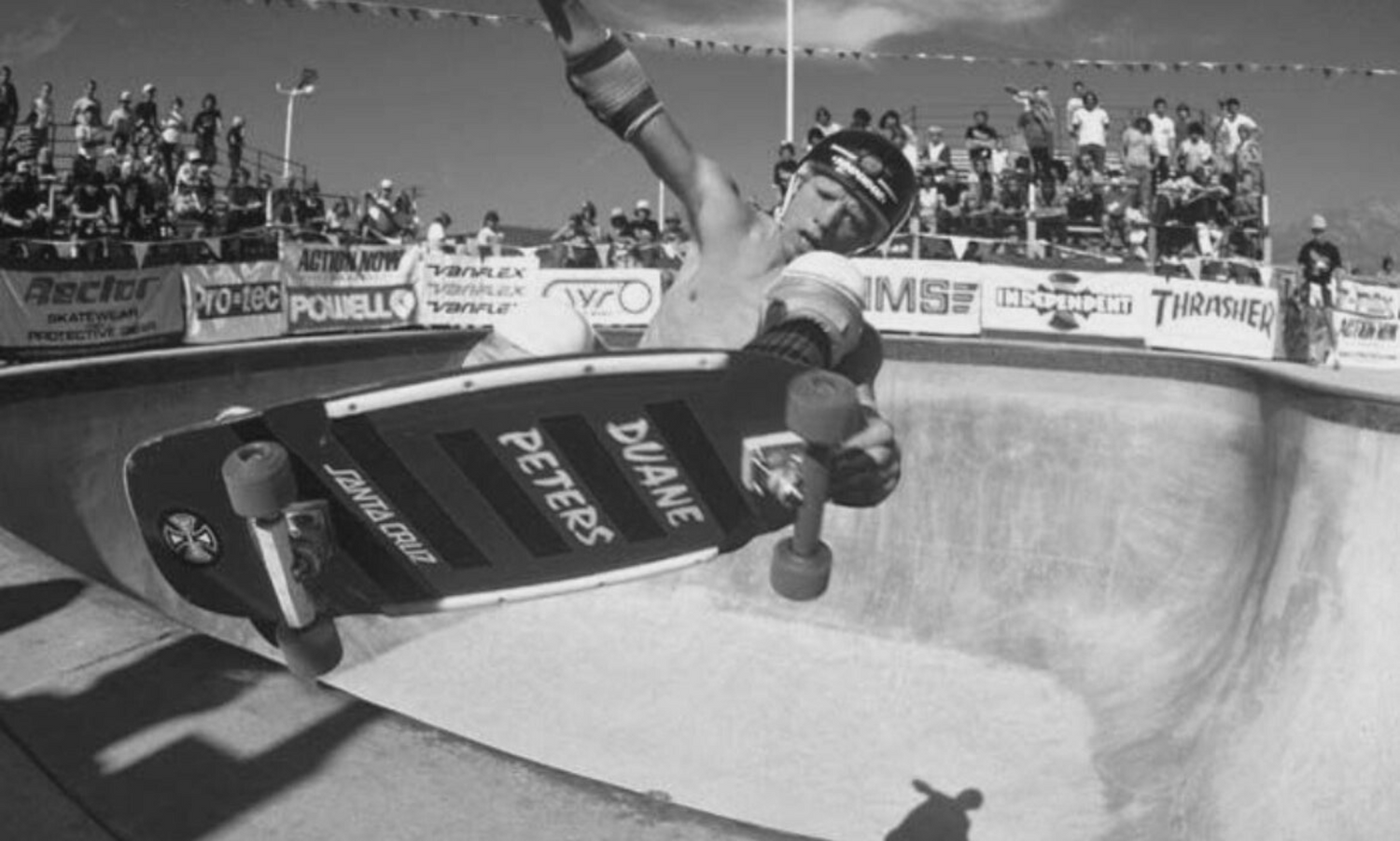 Duane Peters airs above a contest bowl as spectators watch from bleachers with sponsor banners.