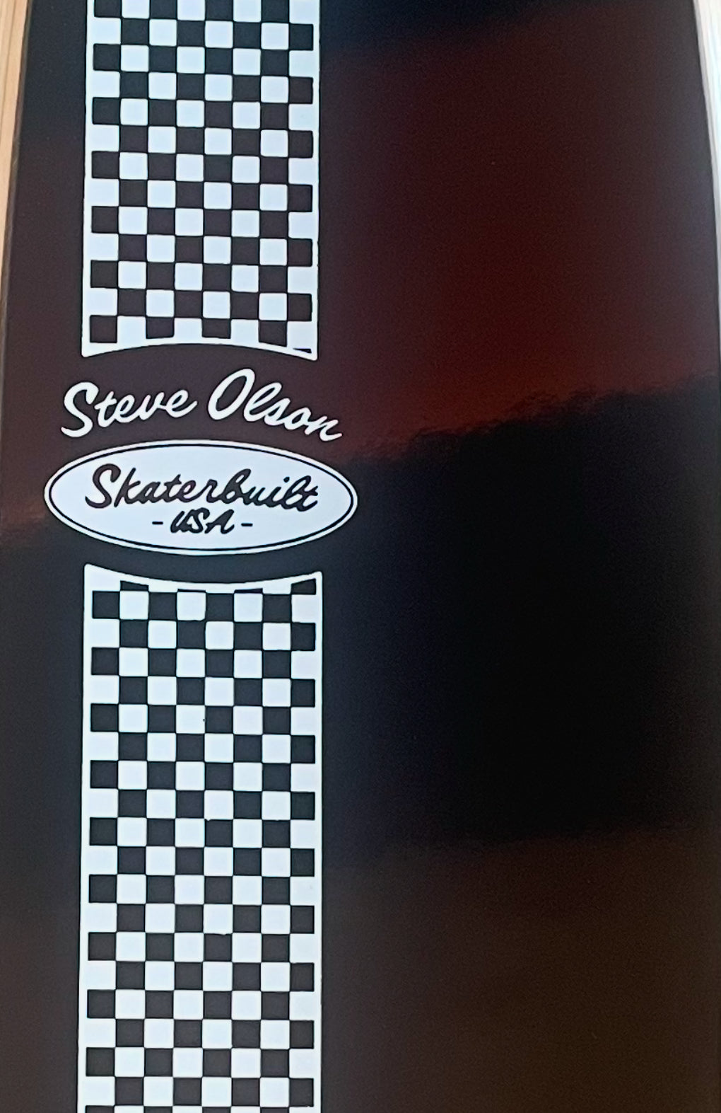 Closeup of Skaterbuilt x Steve Olson Noserider longboard, checkered stripe with Skaterbuilt and Steve Olson logos