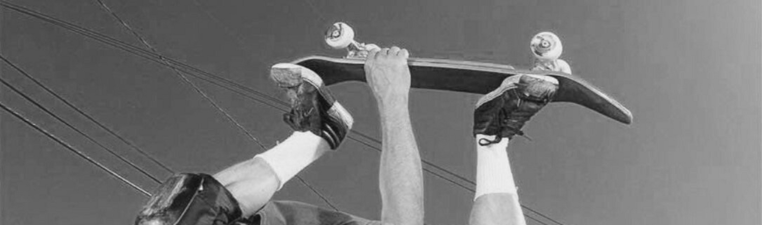 Skater holds board overhead during air with power lines in view, banner introducing SkaterBuilt Parts on All Products.