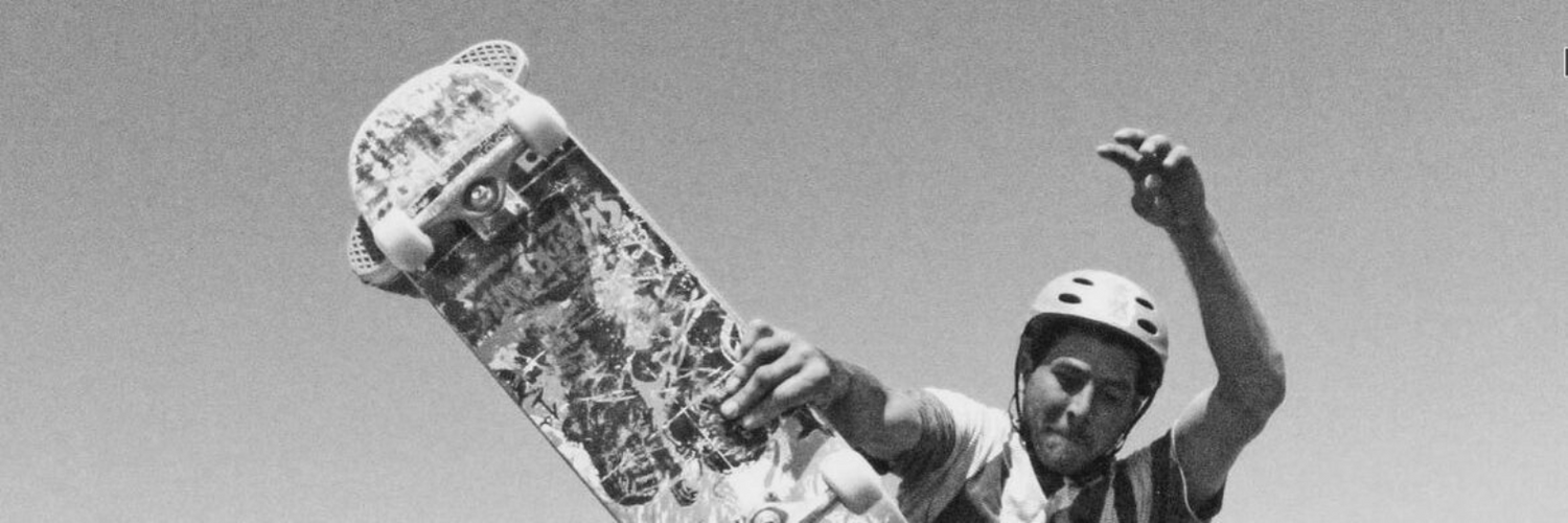 Close-up of skater grabbing Skaterbuilt board mid-air against clear sky, banner for SkaterBuilt Skate Parts.